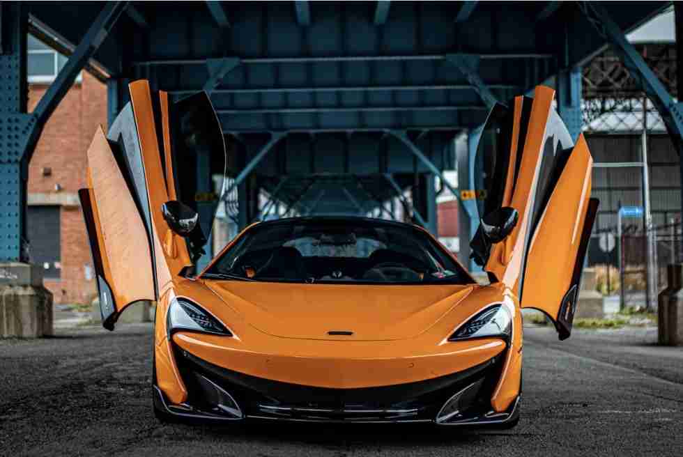 A yellow sports car is parked on a city street flanked by elegant buildings with large windows and arched entrances.